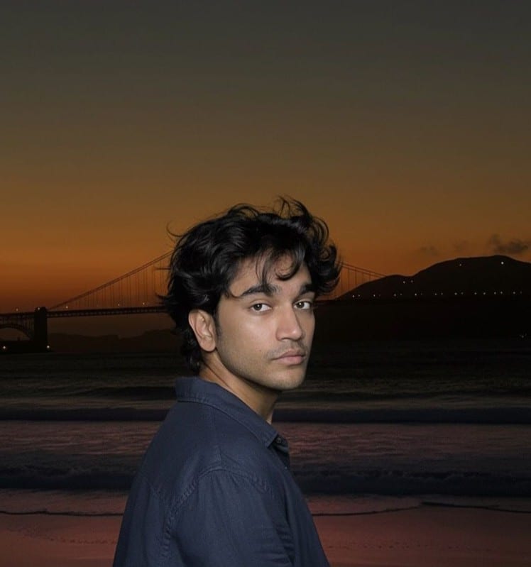 Ezaz Ahamad on the shore below the Golden Gate Bridge at dusk, looking over his shoulder at the camera